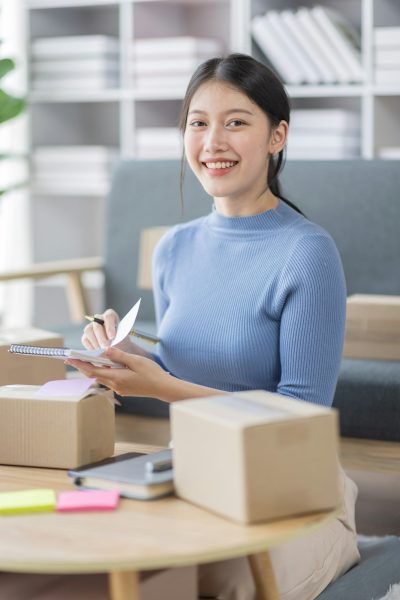 Asian business woman on sofa using a laptop computer checking customer order online shipping boxes a