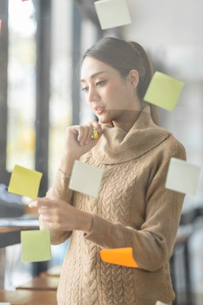 Business Asian woman meeting at office and use post it notes in glass wall to share idea. Brainstorm