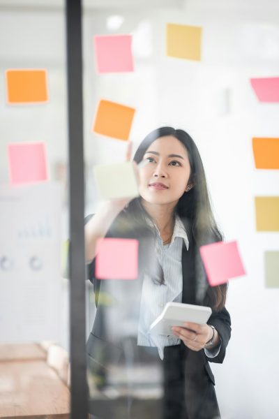 Young Serious Asian Creative team use post it notes to share idea sticky note on glass wall. Asian